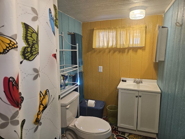 bathroom with toilet, wood walls, and vanity