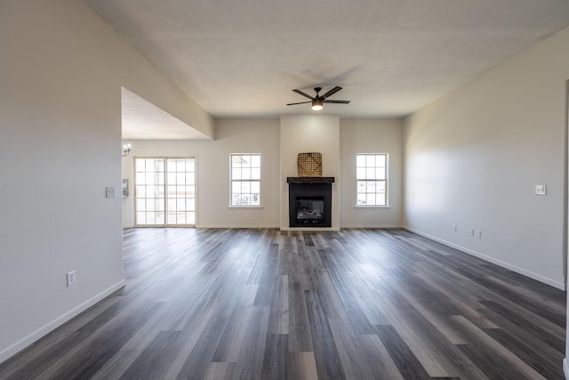 unfurnished living room with a glass covered fireplace, dark wood finished floors, and baseboards