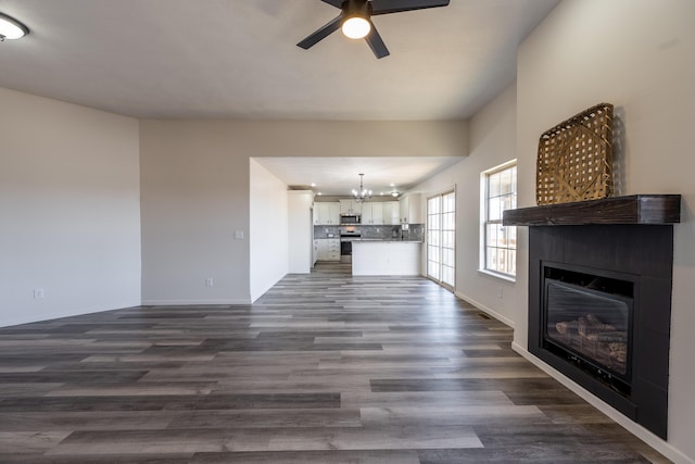 unfurnished living room featuring dark wood-style floors, ceiling fan with notable chandelier, and a glass covered fireplace