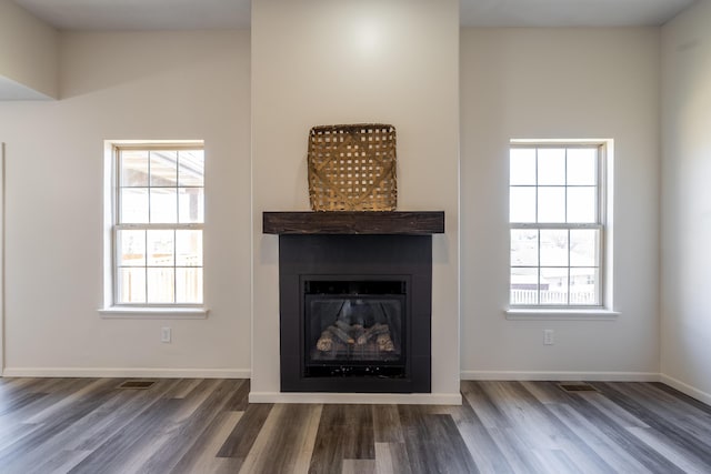 unfurnished living room featuring a glass covered fireplace, visible vents, baseboards, and wood finished floors