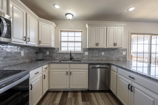 kitchen with dark wood-style flooring, stainless steel appliances, decorative backsplash, white cabinets, and a sink