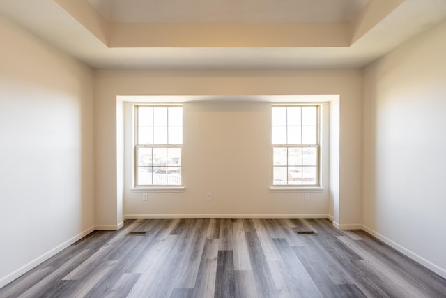 spare room with a tray ceiling, wood finished floors, visible vents, and baseboards