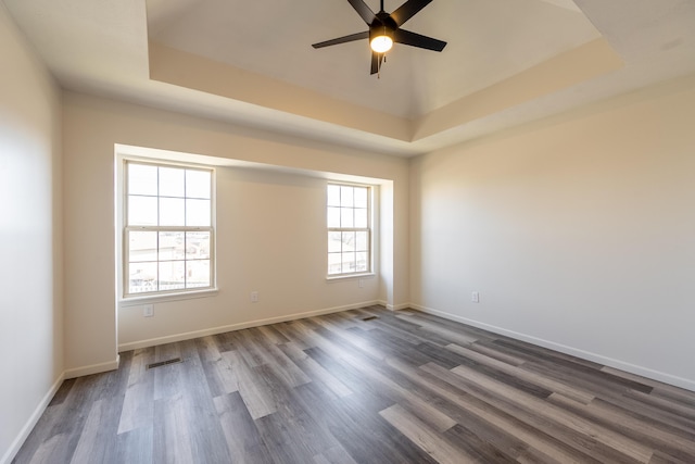 empty room featuring ceiling fan, a raised ceiling, dark wood finished floors, and baseboards