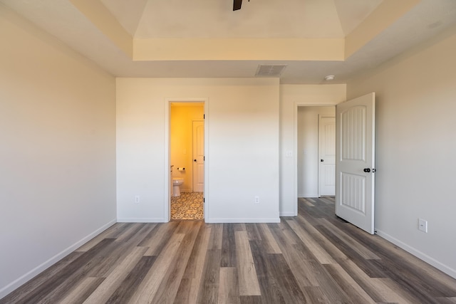 unfurnished bedroom featuring dark wood-style floors, a tray ceiling, visible vents, and baseboards