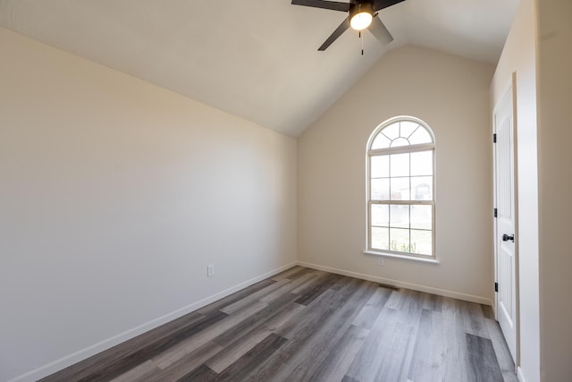 empty room with baseboards, visible vents, a ceiling fan, dark wood-style floors, and vaulted ceiling