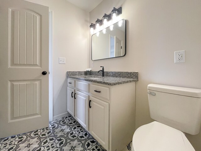 half bath featuring tile patterned flooring, baseboards, vanity, and toilet