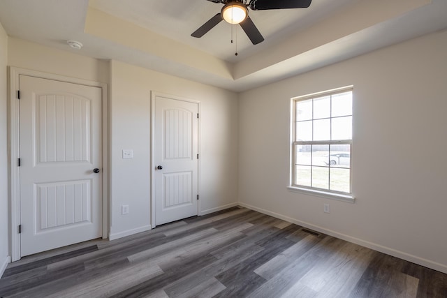 unfurnished bedroom featuring wood finished floors, visible vents, baseboards, a closet, and a tray ceiling