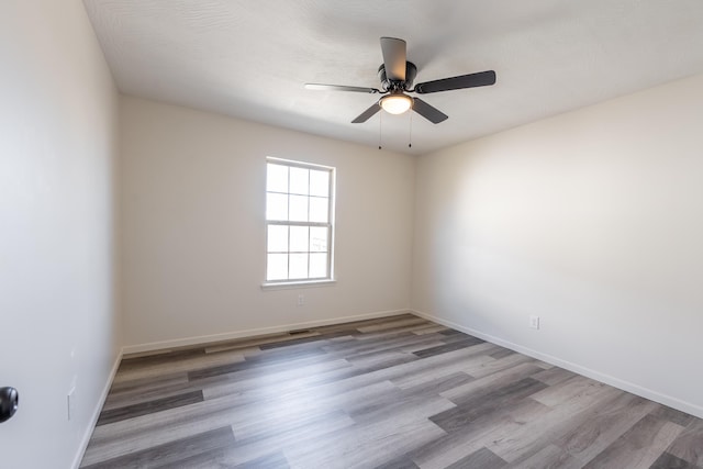 spare room with a ceiling fan, visible vents, baseboards, and wood finished floors