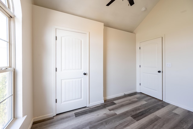 unfurnished bedroom featuring vaulted ceiling, multiple windows, wood finished floors, and baseboards