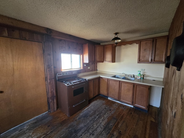 kitchen featuring dark wood-style flooring, brown cabinets, light countertops, a sink, and gas range