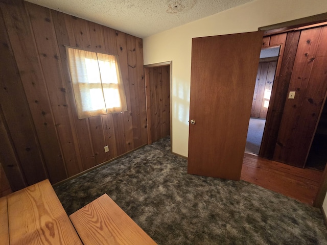 bedroom with a textured ceiling, carpet floors, wood walls, and lofted ceiling