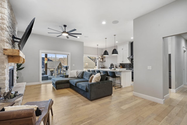 living room with a ceiling fan, baseboards, a fireplace, and light wood finished floors