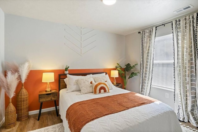 bedroom with wood finished floors, visible vents, and baseboards