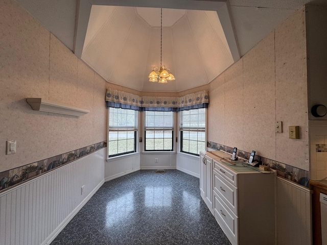 unfurnished dining area featuring an inviting chandelier, wainscoting, vaulted ceiling, baseboards, and wallpapered walls