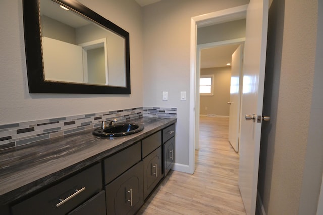 bathroom featuring wood finished floors, backsplash, vanity, and baseboards