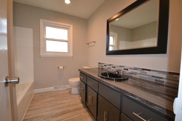 bathroom featuring toilet, wood finished floors, visible vents, baseboards, and decorative backsplash