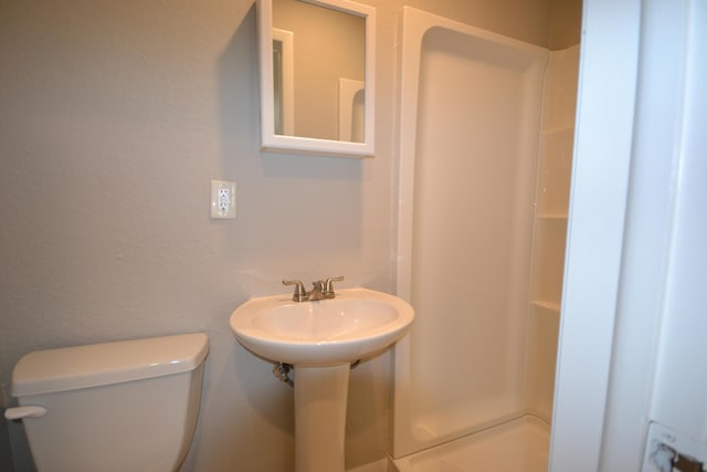 bathroom featuring toilet, a shower, and a sink