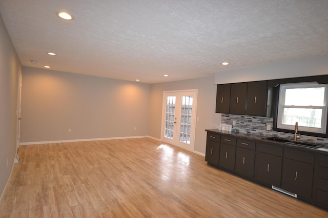 kitchen featuring tasteful backsplash, dark countertops, a healthy amount of sunlight, a sink, and light wood-type flooring