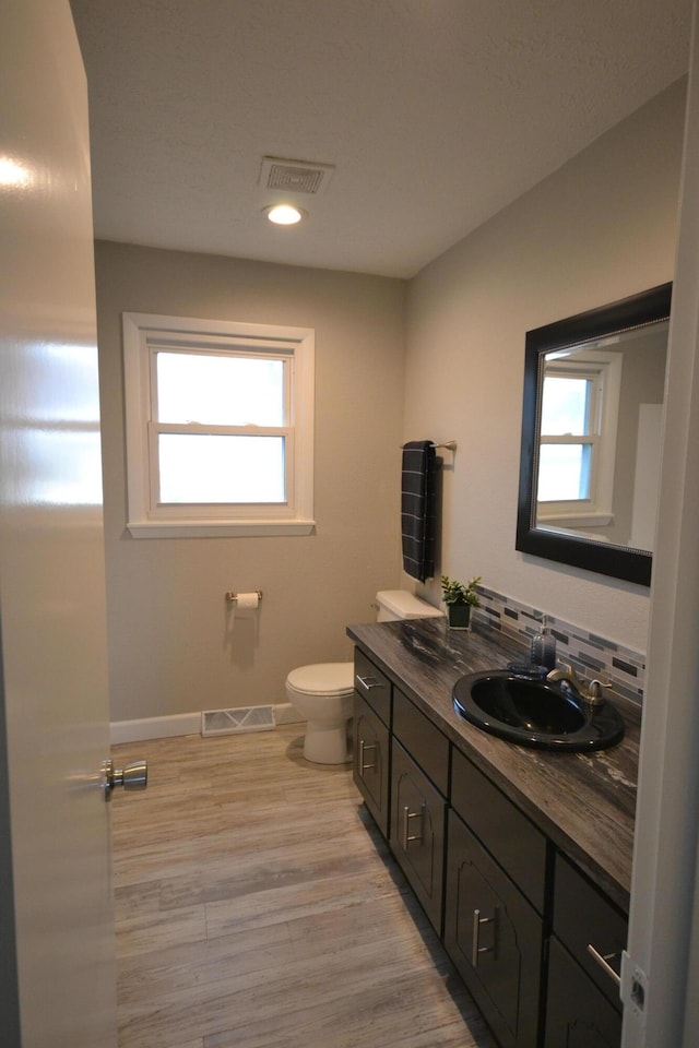 bathroom featuring a healthy amount of sunlight, toilet, decorative backsplash, and wood finished floors