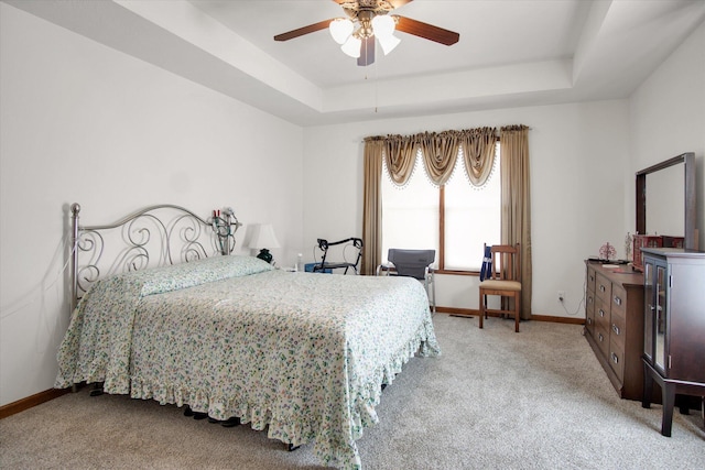 bedroom with a ceiling fan, a tray ceiling, carpet, and baseboards