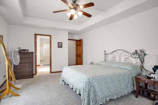 bedroom featuring a tray ceiling, carpet, ensuite bathroom, ceiling fan, and baseboards