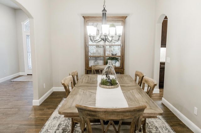 dining area featuring arched walkways, dark wood-style flooring, a chandelier, and baseboards