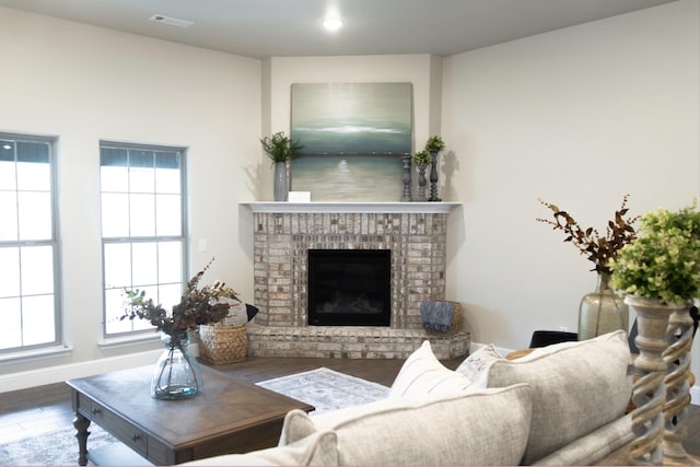 living room featuring a brick fireplace, wood finished floors, visible vents, and baseboards