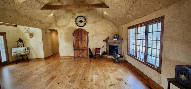 interior space featuring arched walkways, lofted ceiling with beams, hardwood / wood-style flooring, a wood stove, and a fireplace