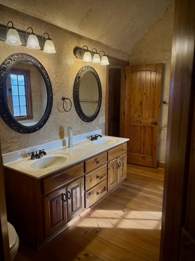 bathroom featuring lofted ceiling, hardwood / wood-style flooring, double vanity, and a sink