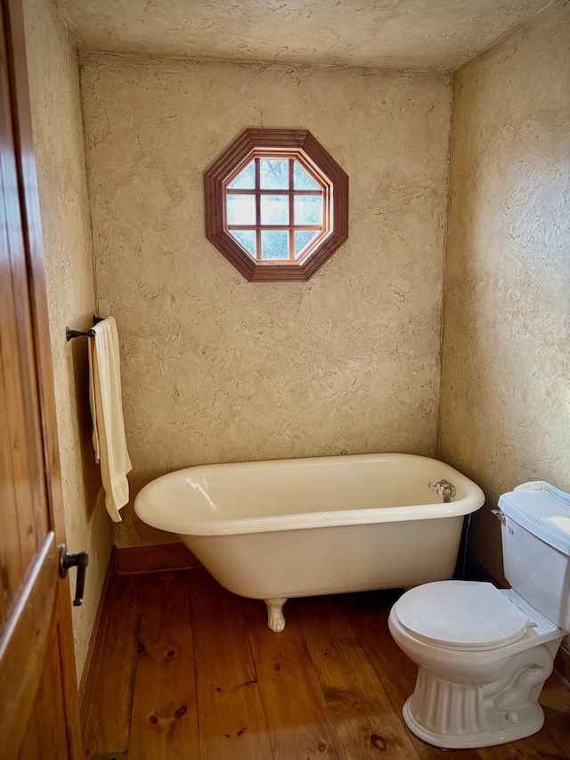 full bathroom featuring a soaking tub, a textured wall, hardwood / wood-style floors, and toilet