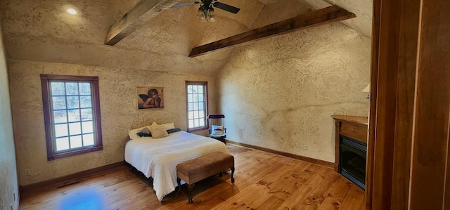 bedroom featuring light wood-type flooring, multiple windows, and a glass covered fireplace