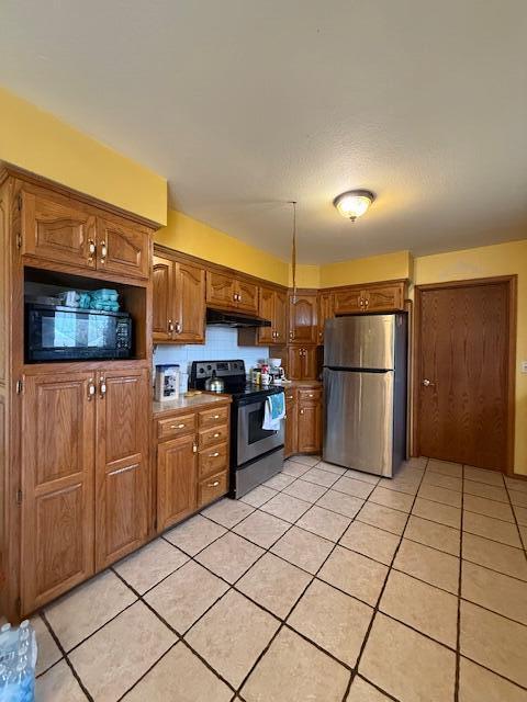 kitchen with appliances with stainless steel finishes, brown cabinets, under cabinet range hood, and light tile patterned floors