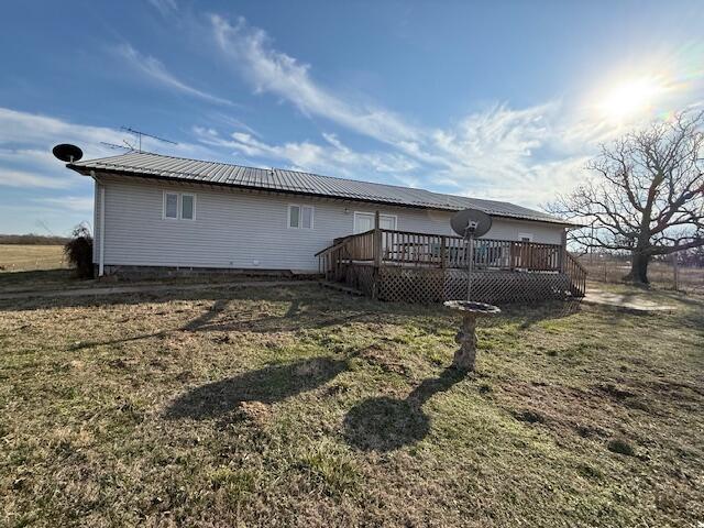 back of house featuring metal roof, a deck, and a lawn