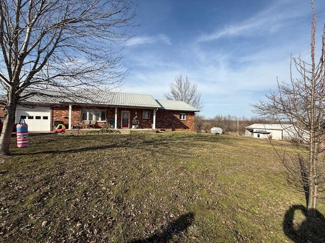 view of front of property with a front yard, covered porch, brick siding, and an attached garage