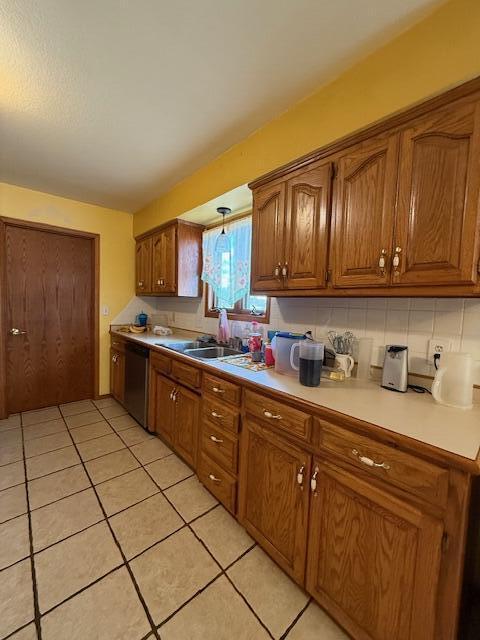 kitchen with light tile patterned floors, tasteful backsplash, brown cabinetry, light countertops, and stainless steel dishwasher