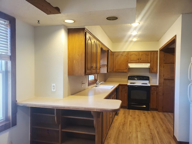 kitchen with light countertops, electric range oven, brown cabinetry, a sink, and under cabinet range hood