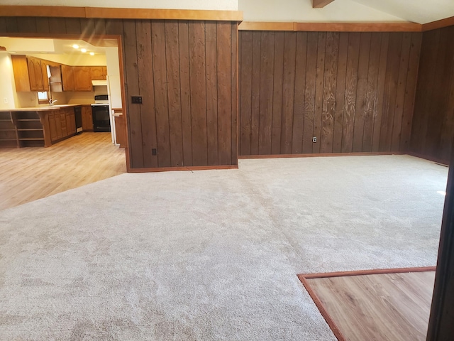 unfurnished living room featuring light carpet, a sink, and wooden walls