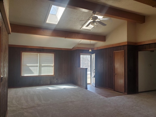 empty room with lofted ceiling with skylight, carpet, ceiling fan, and a textured ceiling