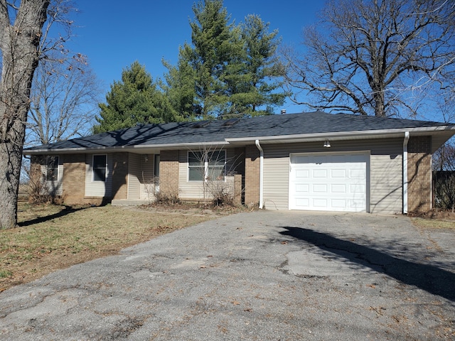 ranch-style house with driveway, brick siding, roof with shingles, and an attached garage