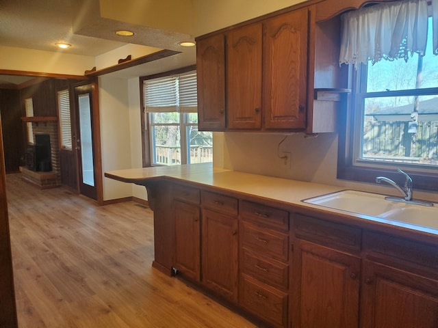 kitchen featuring a fireplace, a sink, light countertops, brown cabinets, and light wood finished floors