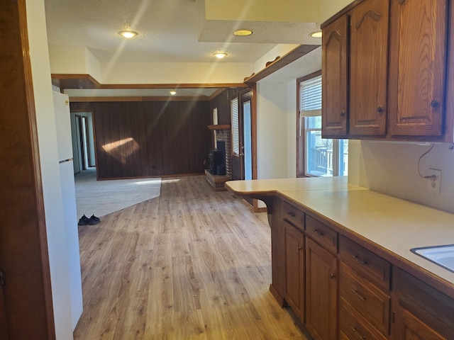 kitchen with brown cabinetry, light wood-style flooring, light countertops, a brick fireplace, and recessed lighting