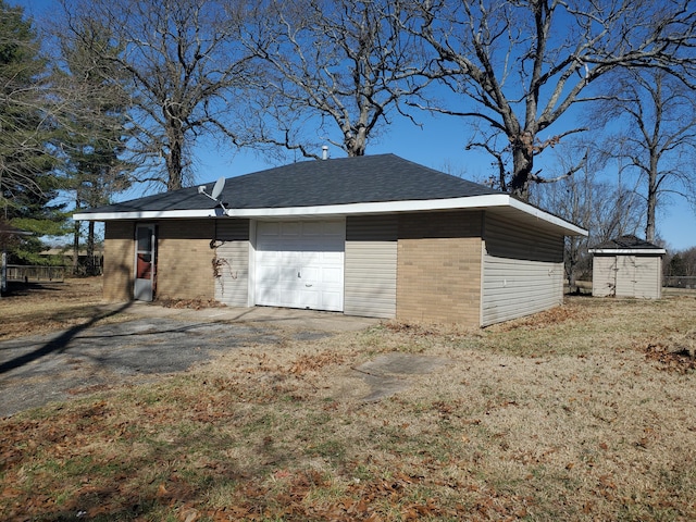 exterior space featuring brick siding, roof with shingles, an attached garage, an outdoor structure, and driveway