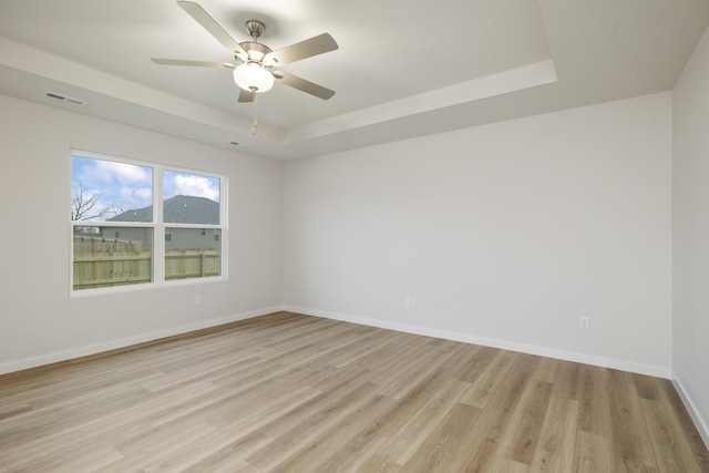 empty room with visible vents, baseboards, light wood finished floors, a raised ceiling, and ceiling fan