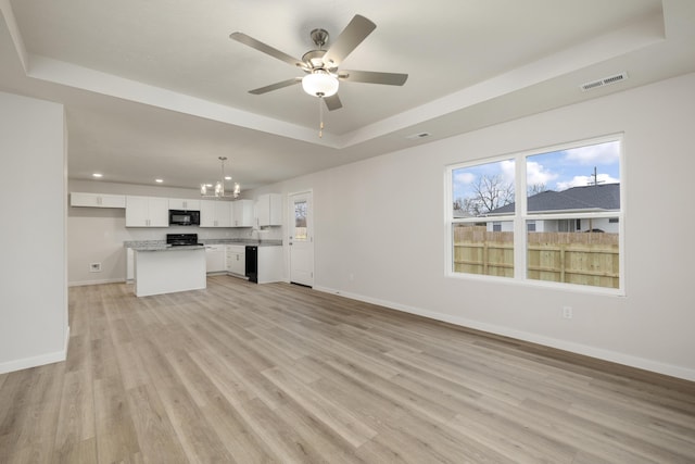 unfurnished living room featuring ceiling fan with notable chandelier, a raised ceiling, baseboards, and light wood-type flooring