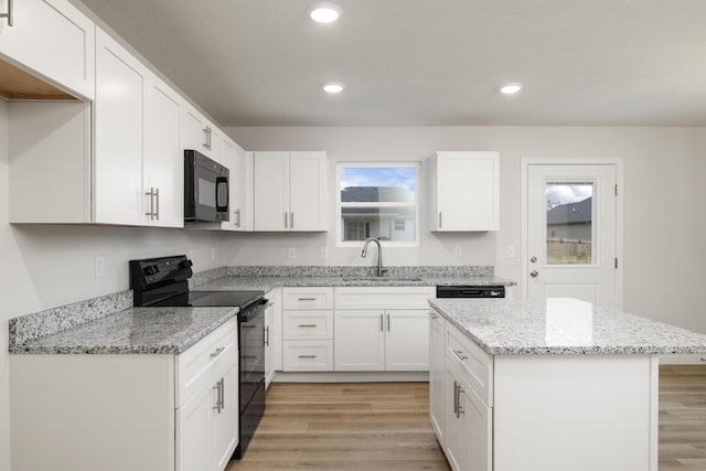 kitchen with light wood finished floors, a kitchen island, a sink, black appliances, and white cabinetry