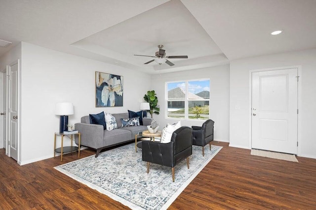 living area with baseboards, visible vents, dark wood-style floors, ceiling fan, and a tray ceiling