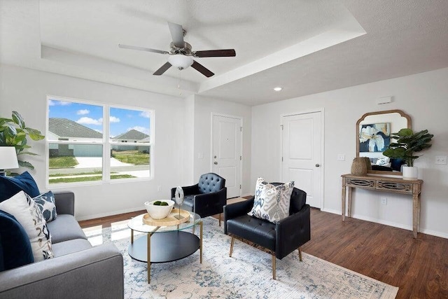 living room featuring a ceiling fan, baseboards, a raised ceiling, and wood finished floors