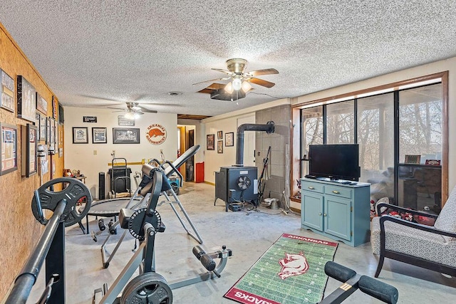 workout area with a wood stove, a ceiling fan, and a textured ceiling