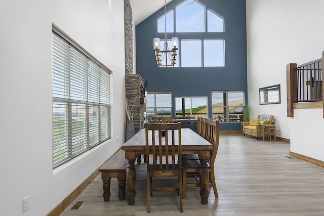 dining space with visible vents, a high ceiling, wood finished floors, a chandelier, and baseboards