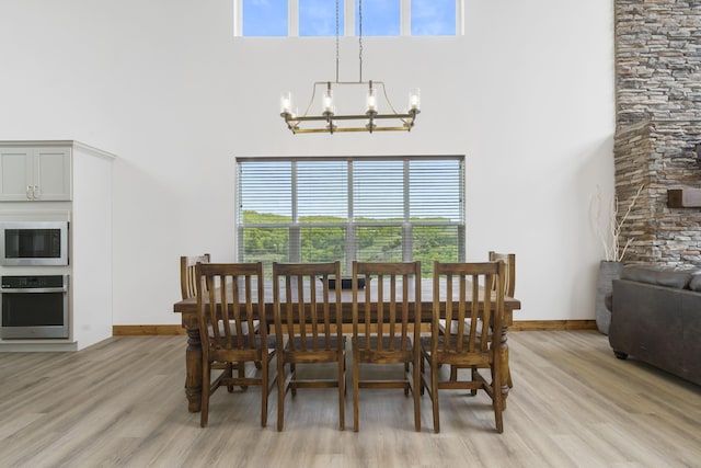 dining space with a towering ceiling, light wood-style flooring, baseboards, and a notable chandelier